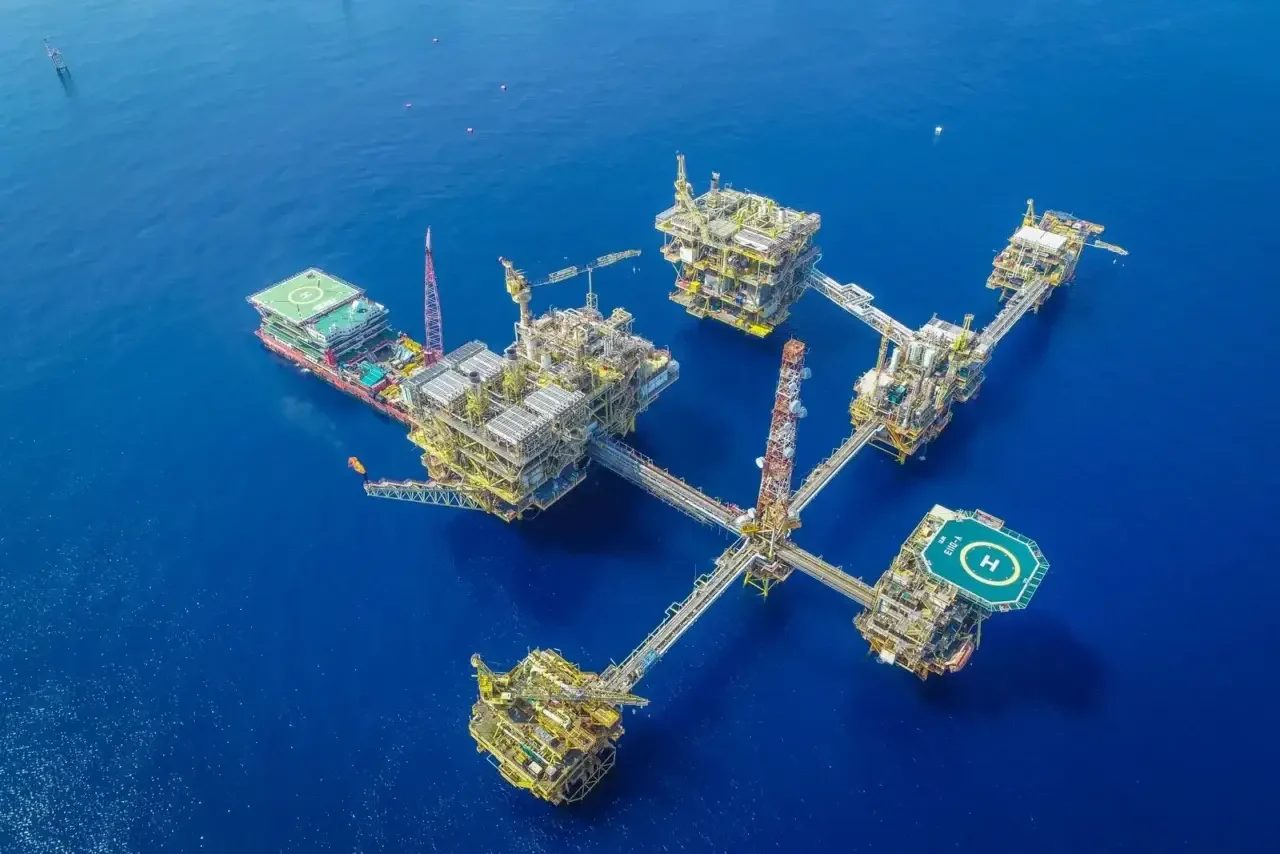 Drone shot of a large, complex offshore oil platform in deep blue ocean waters.