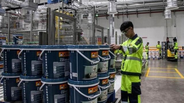 Suasana aktivitas di dalam pabrik manufaktur dengan mesin produksi yang sedang beroperasi.