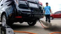 Deretan kendaraan listrik yang terparkir di jalanan Jakarta dengan latar belakang gedung tinggi dan polusi udara.